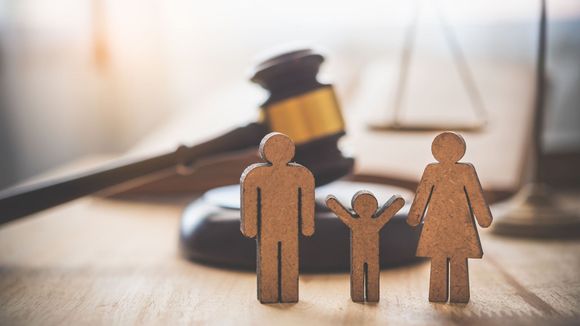 Figuras de madera de una familia frente al mazo de un juez sobre un escritorio, simbolizando el derecho de familia o una disputa por la custodia.