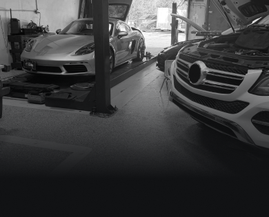 Two luxury cars parked in a garage, one silver sports car on the left and a black Mercedes on the right | Master Auto Collision