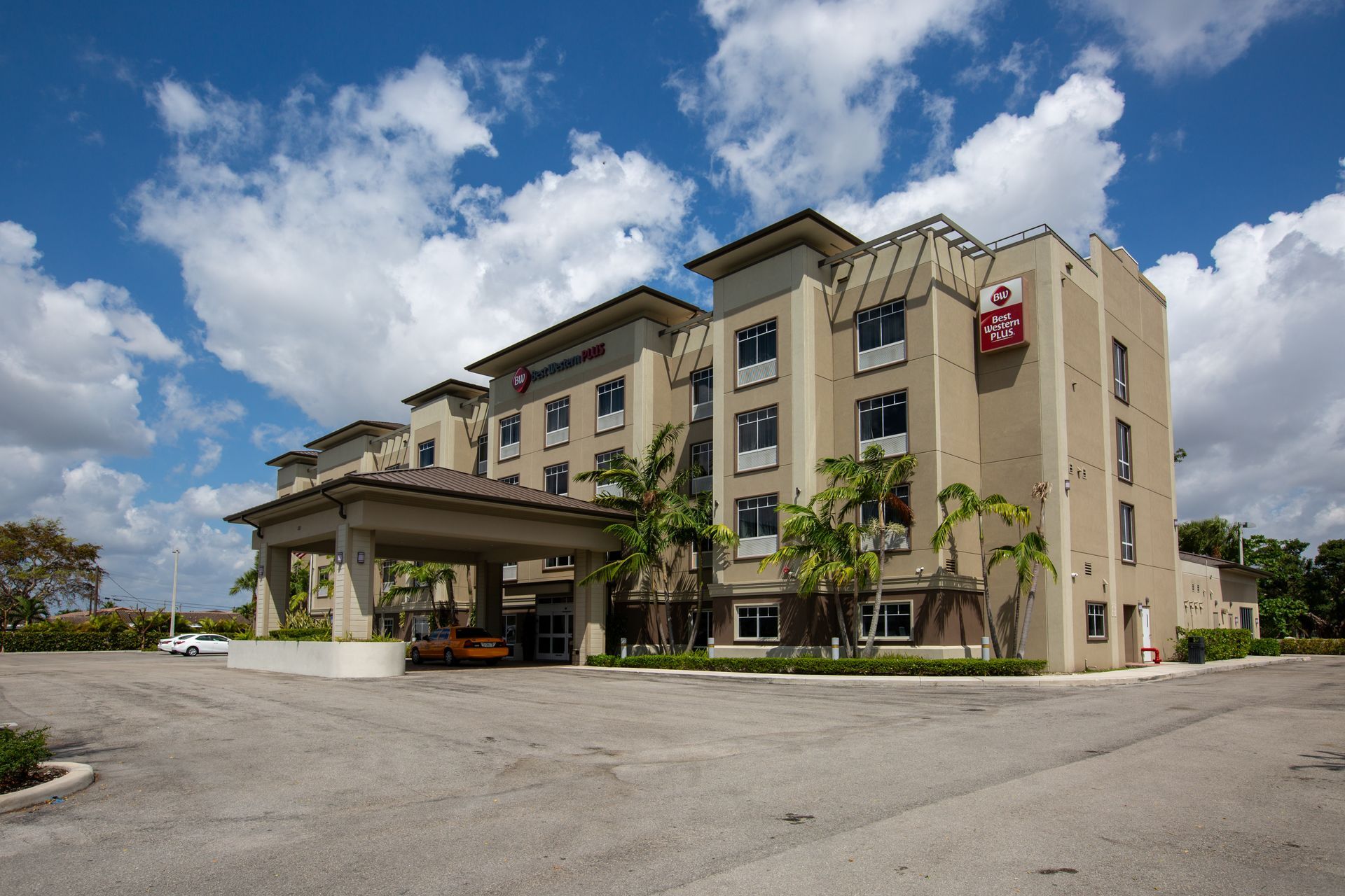 Hotel exterior with a covered entrance under a blue sky with clouds.