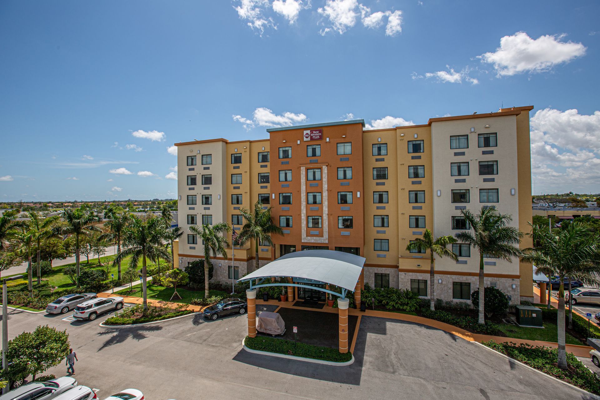 Hotel exterior with a covered entrance, palm trees, and a blue sky.