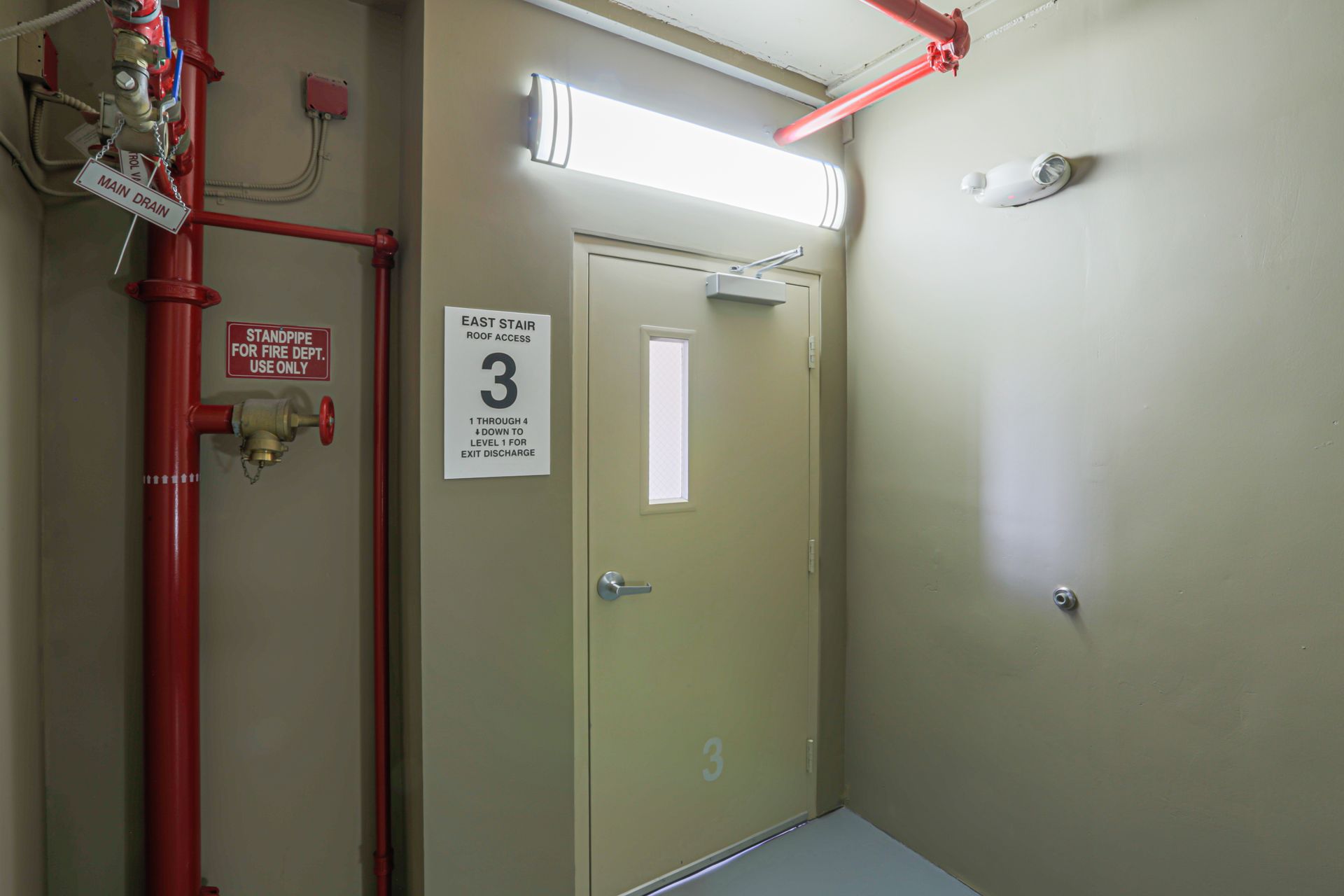 Fire exit on floor 3, with red pipes, door with window, and overhead lighting.
