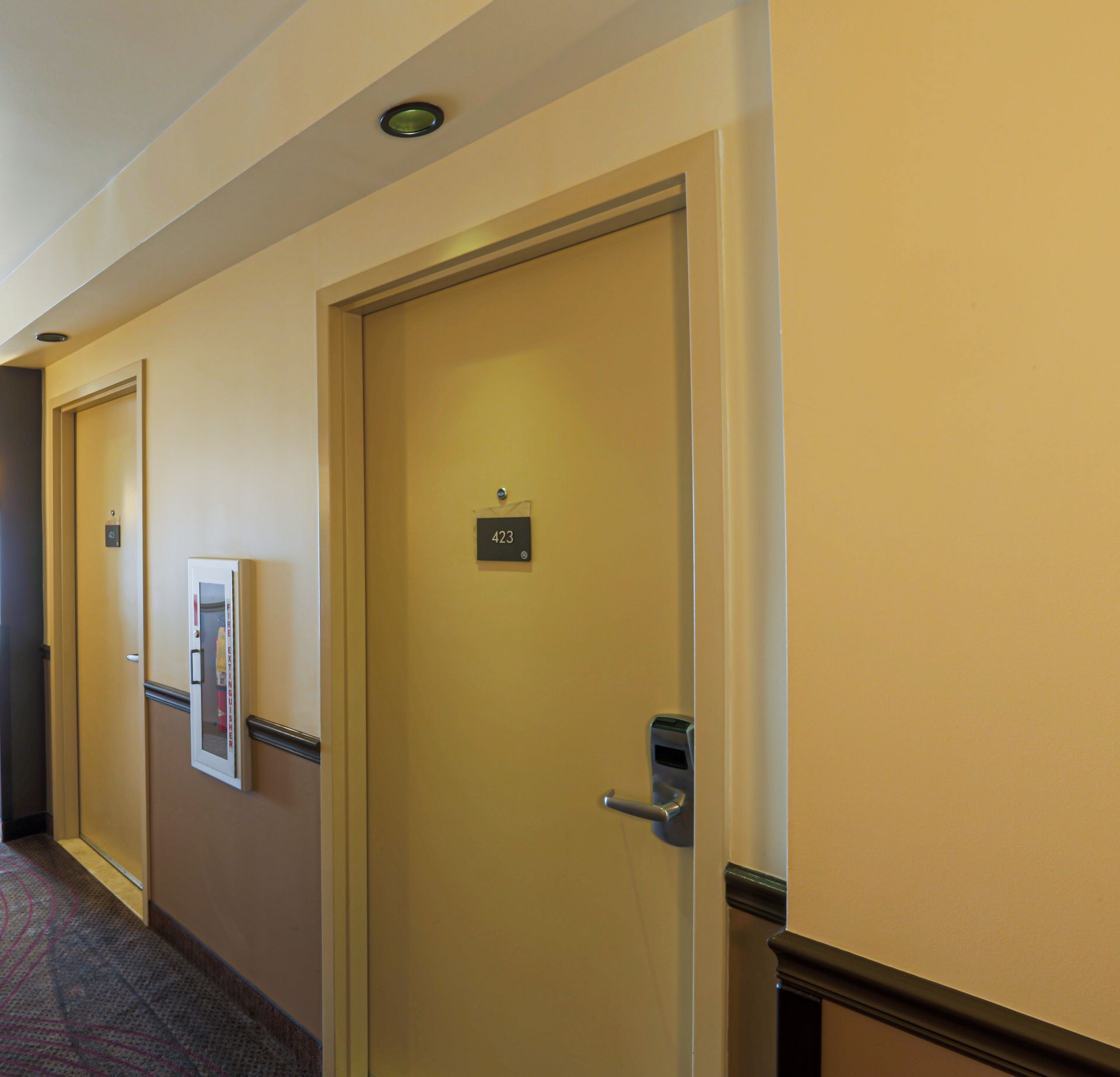 Hotel hallway with beige walls, closed doors, and a fire extinguisher.