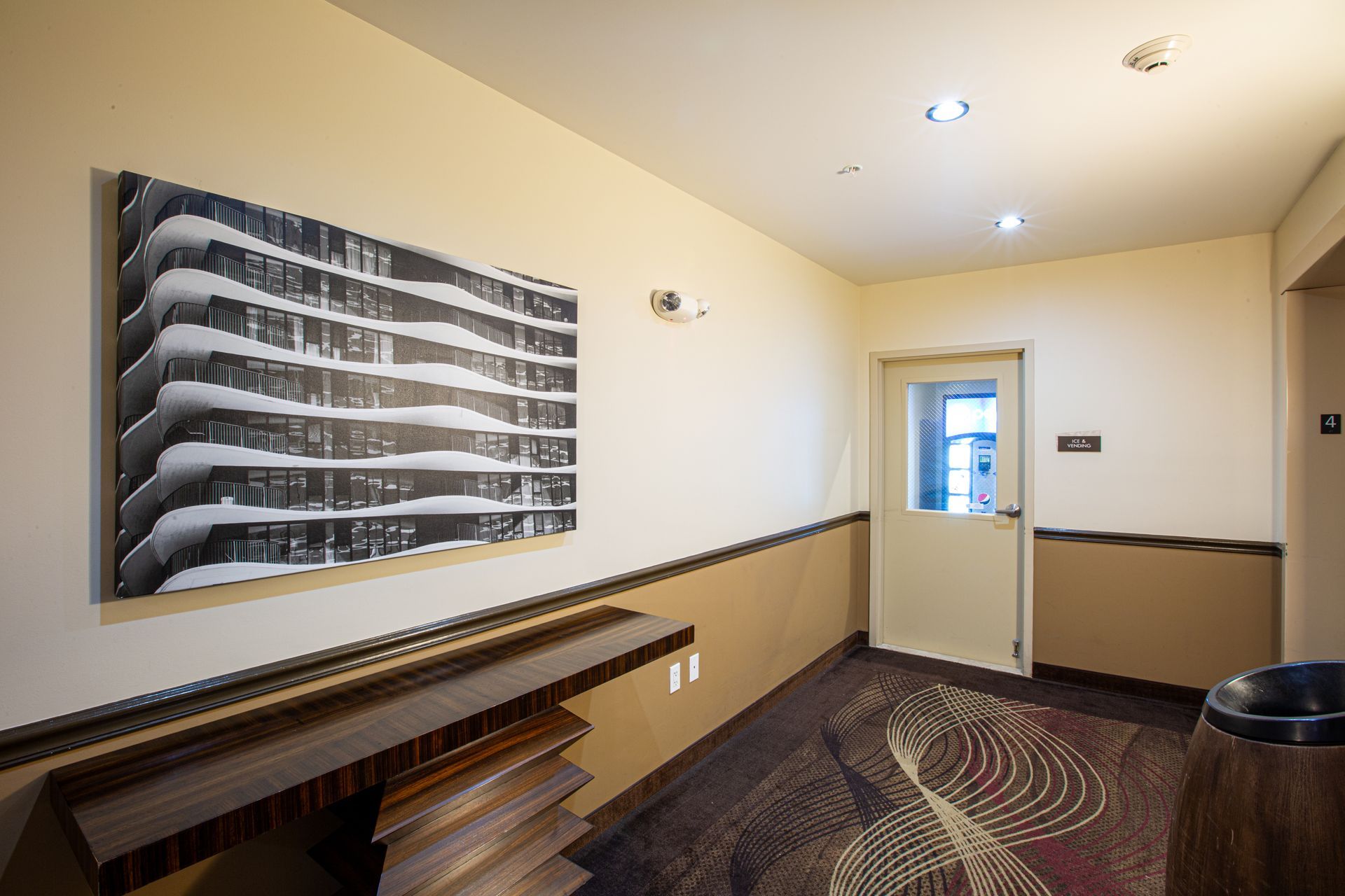 Hallway with art, beige walls, patterned carpet, and a closed door.