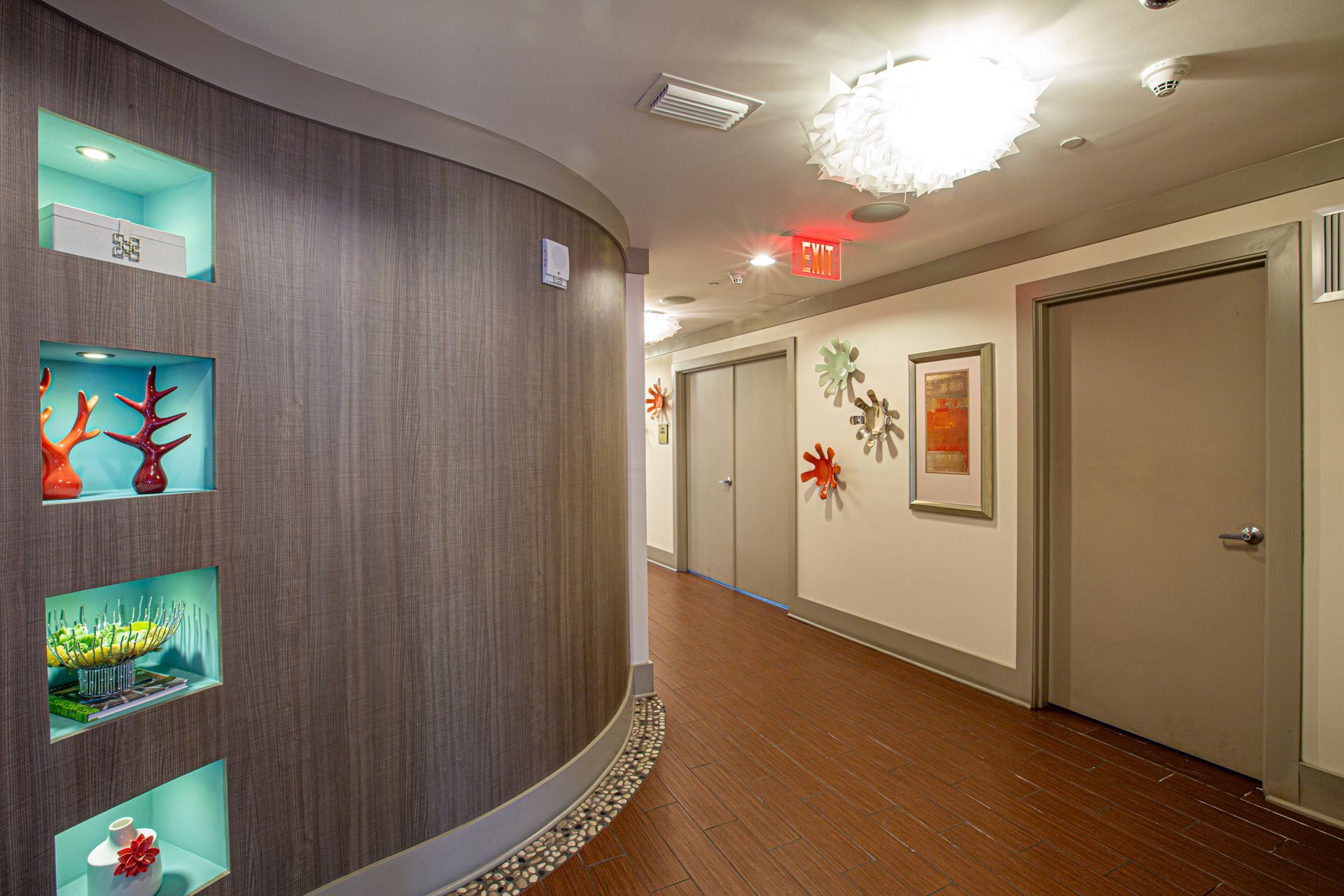 Hallway with curved wood wall featuring recessed display shelves. Doors and artwork line the opposite wall.