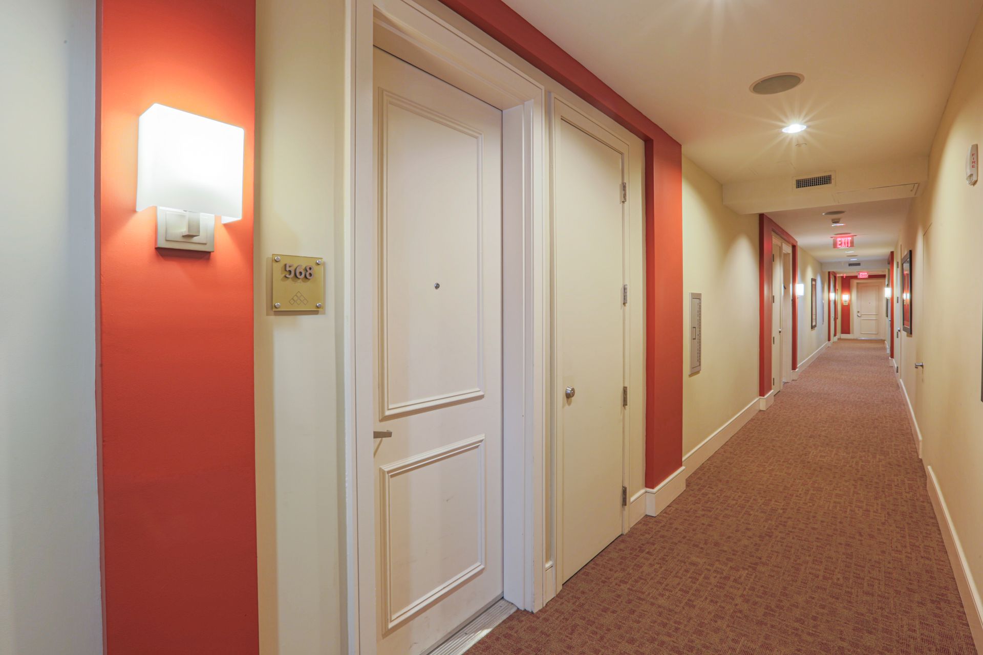 Hallway with red and beige walls, patterned carpet, and closed white doors.
