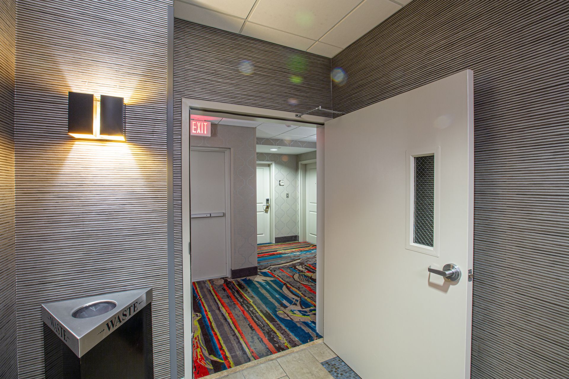 Hallway entrance with patterned wallpaper, door, and a colorful rug.