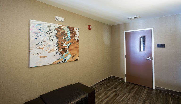 Hallway with abstract art, bench, brown door with window, and wood-look flooring.