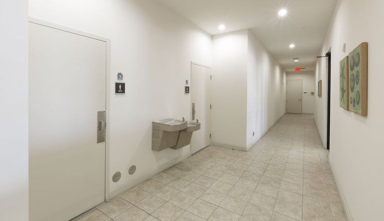 Hallway with white walls, a water fountain, and doors, with a restroom sign.