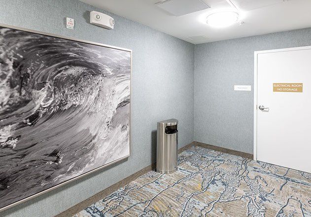 Hallway with wave art, trash can, patterned carpet, and door with sign.