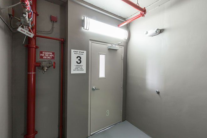 Corridor with door to level 3, red fire pipes, overhead lighting, gray walls.