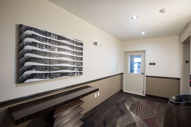 Hallway with artwork and door. Dark wood table, patterned carpet. Beige and brown walls.