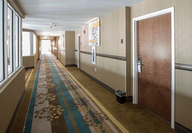 Hotel hallway with patterned carpet, doors, and windows to the left.