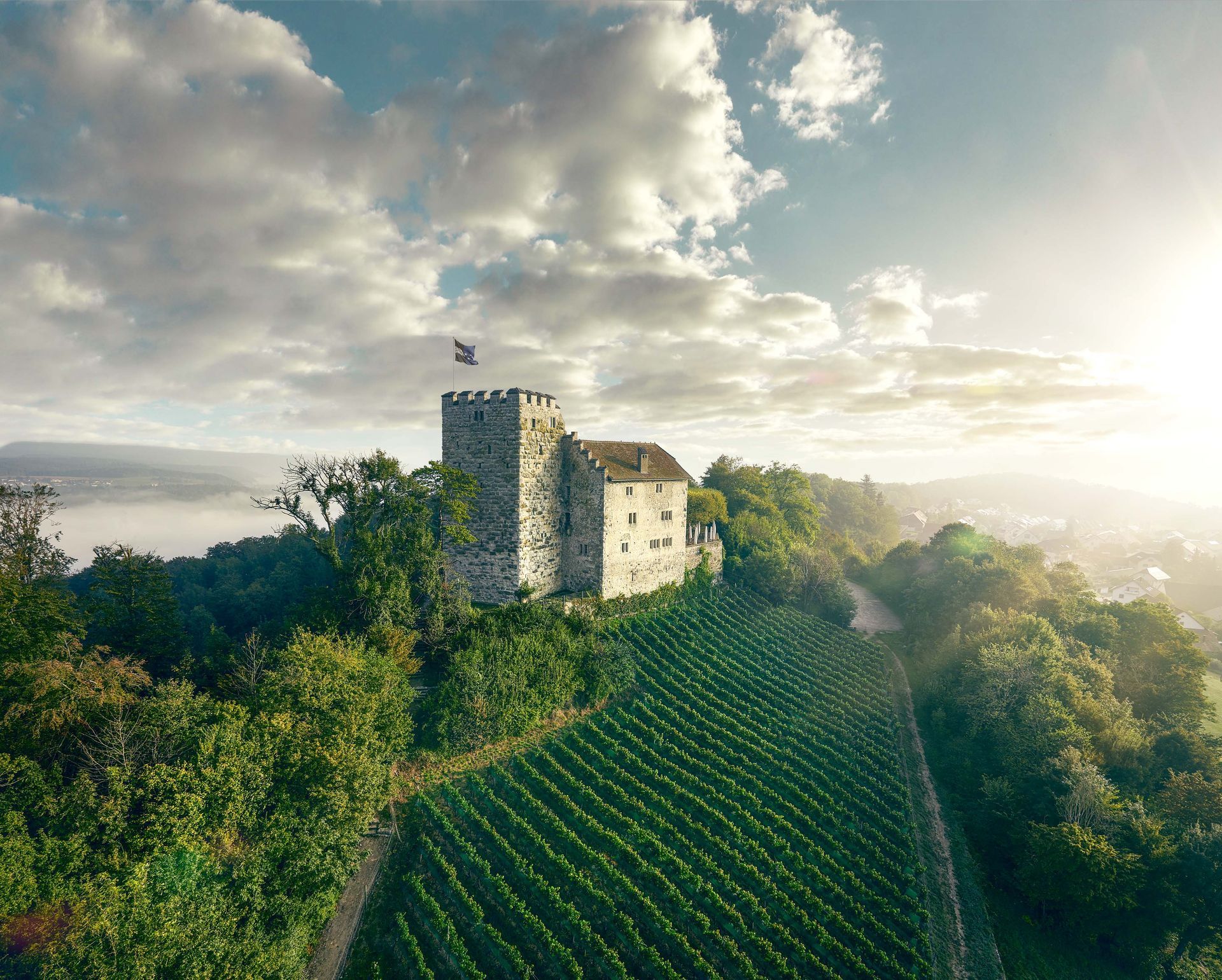Steinturm und Gebäude mit Blick auf üppig grüne Weinberge im Sonnenuntergang bei strahlend blauem Himmel und Wolken