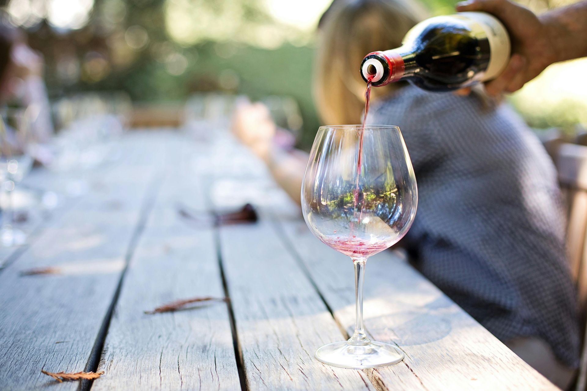 Wein wird auf einem hölzernen Gartentisch in ein Glas eingeschenkt.