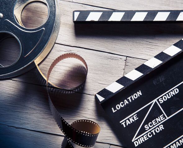 Film reel and clapperboard on a wooden table, with labels for location, take, sound, and director.