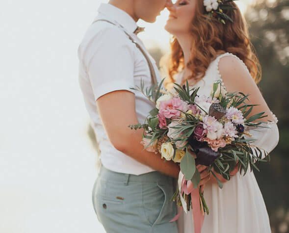 Couple embracing outdoors, holding a pink and white bouquet in soft sunlight