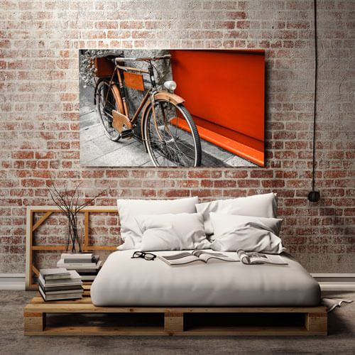 Modern bedroom with a pallet bed and brick wall, featuring a framed orange bicycle photo above the bed