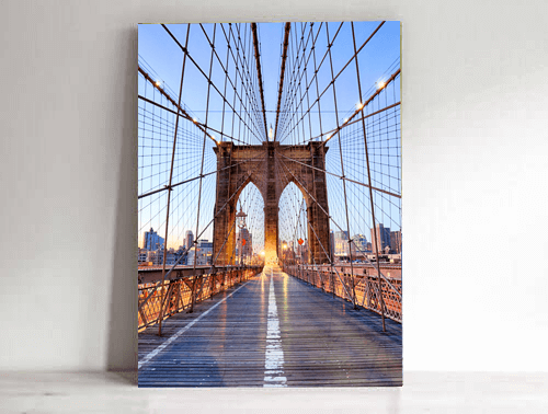 Brooklyn Bridge walkway with glowing cables and Manhattan skyline at sunset