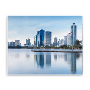 Modern city skyline with tall buildings reflected in calm water at sunrise
