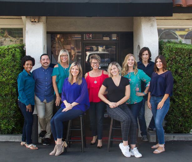 Group of eight people posing outside a building entrance, smiling and seated standing in two rows.