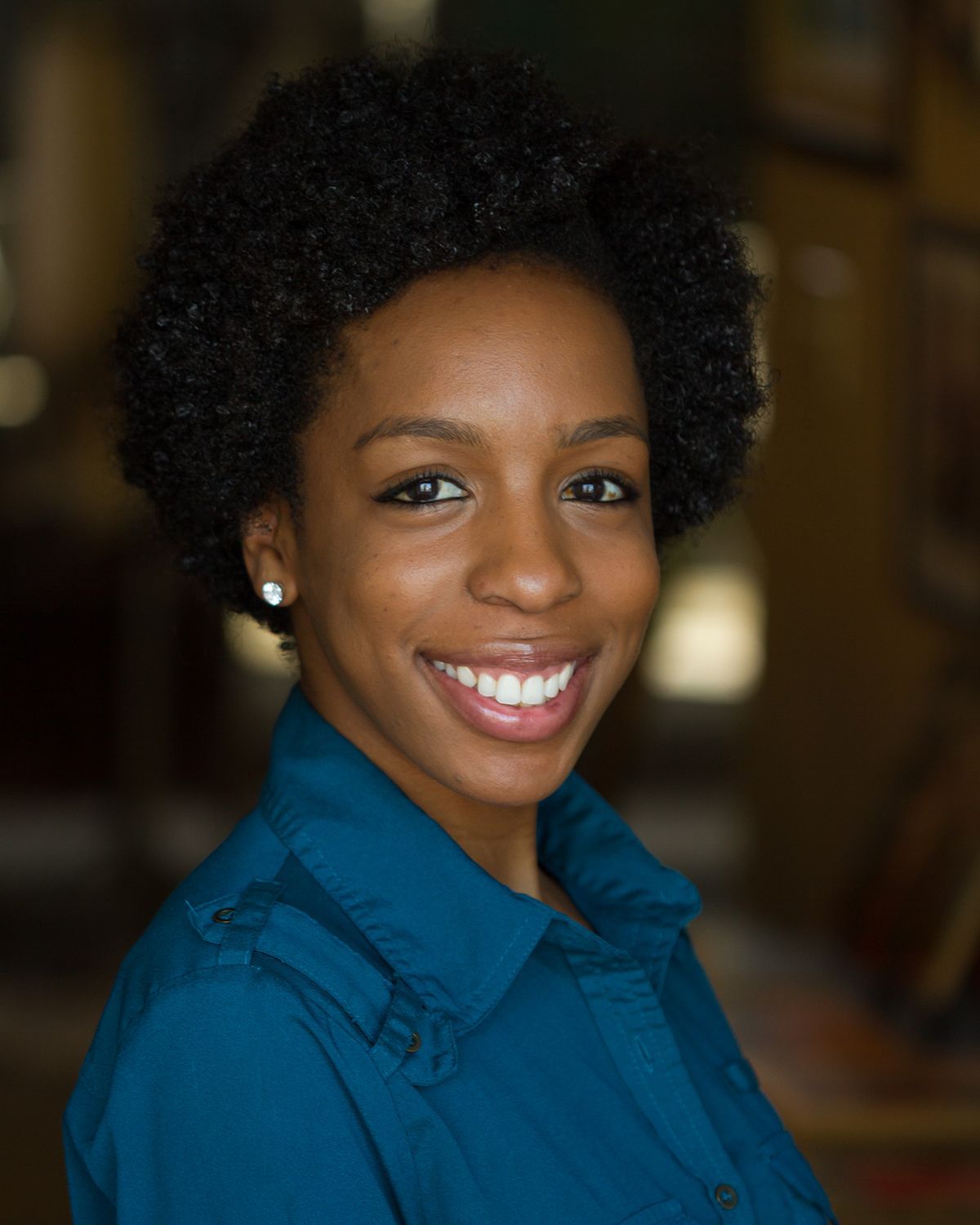 Smiling person in a blue shirt against a softly blurred indoor background