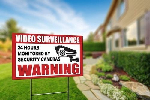 Red warning sign for video surveillance with camera icons in a suburban yard near a house