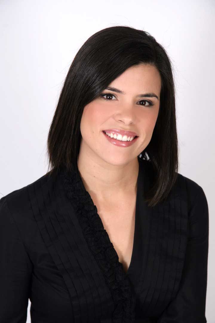 Portrait of a smiling woman with shoulder-length dark hair, wearing a black top against a light background