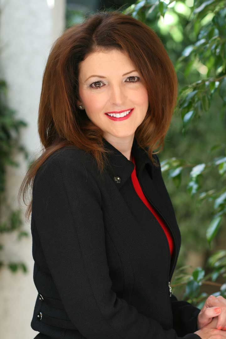 Portrait of a smiling woman in a black blazer against a leafy green background
