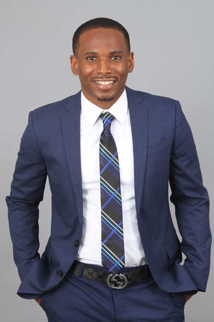 Man in a blue suit and striped tie smiling against a gray background