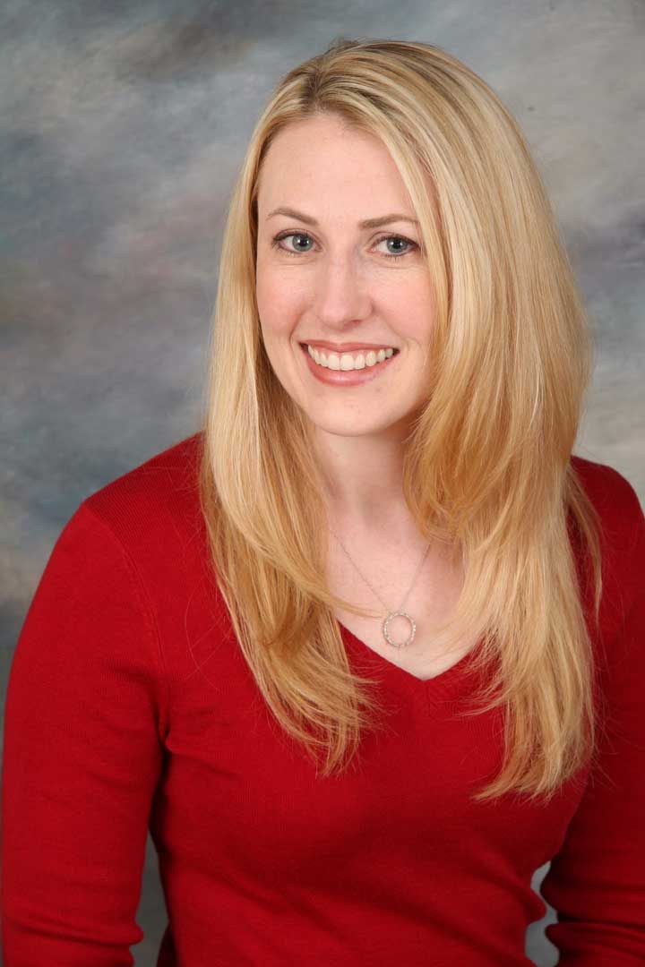 Smiling blonde woman in a red top against a gray studio backdrop
