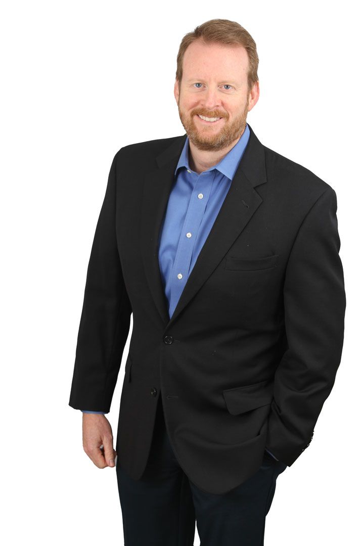 Man in a black suit and blue shirt posing against a white background
