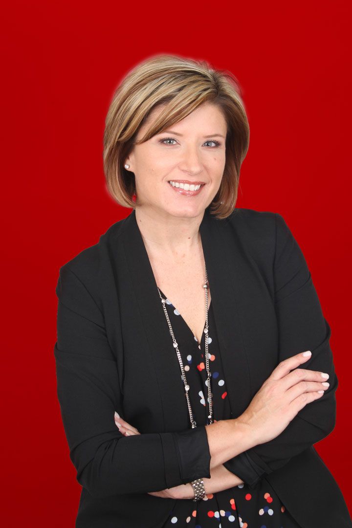 Smiling woman in a black blazer with arms crossed against a red background