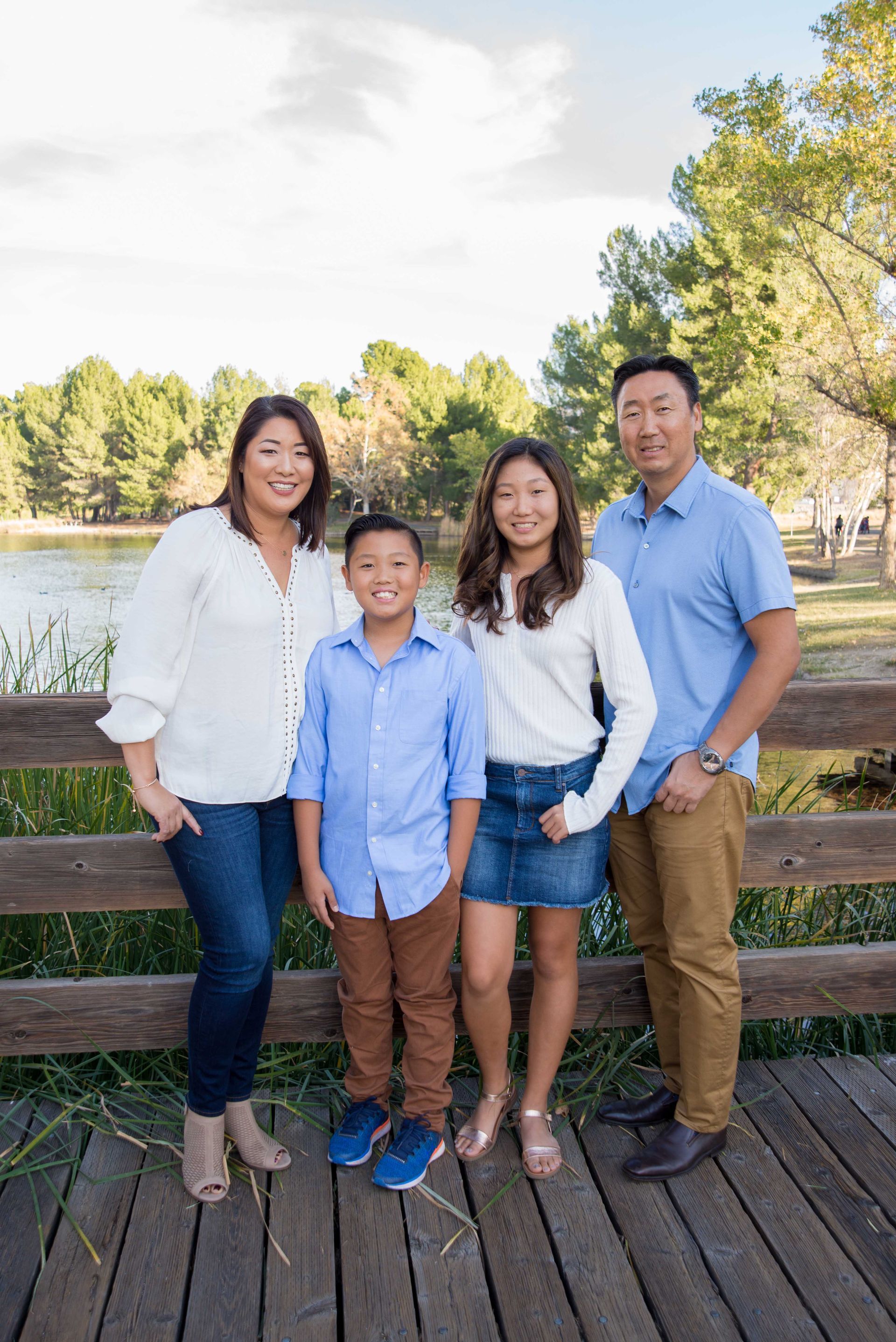 Four people standing on a wooden dock by a lake, smiling in casual clothes.