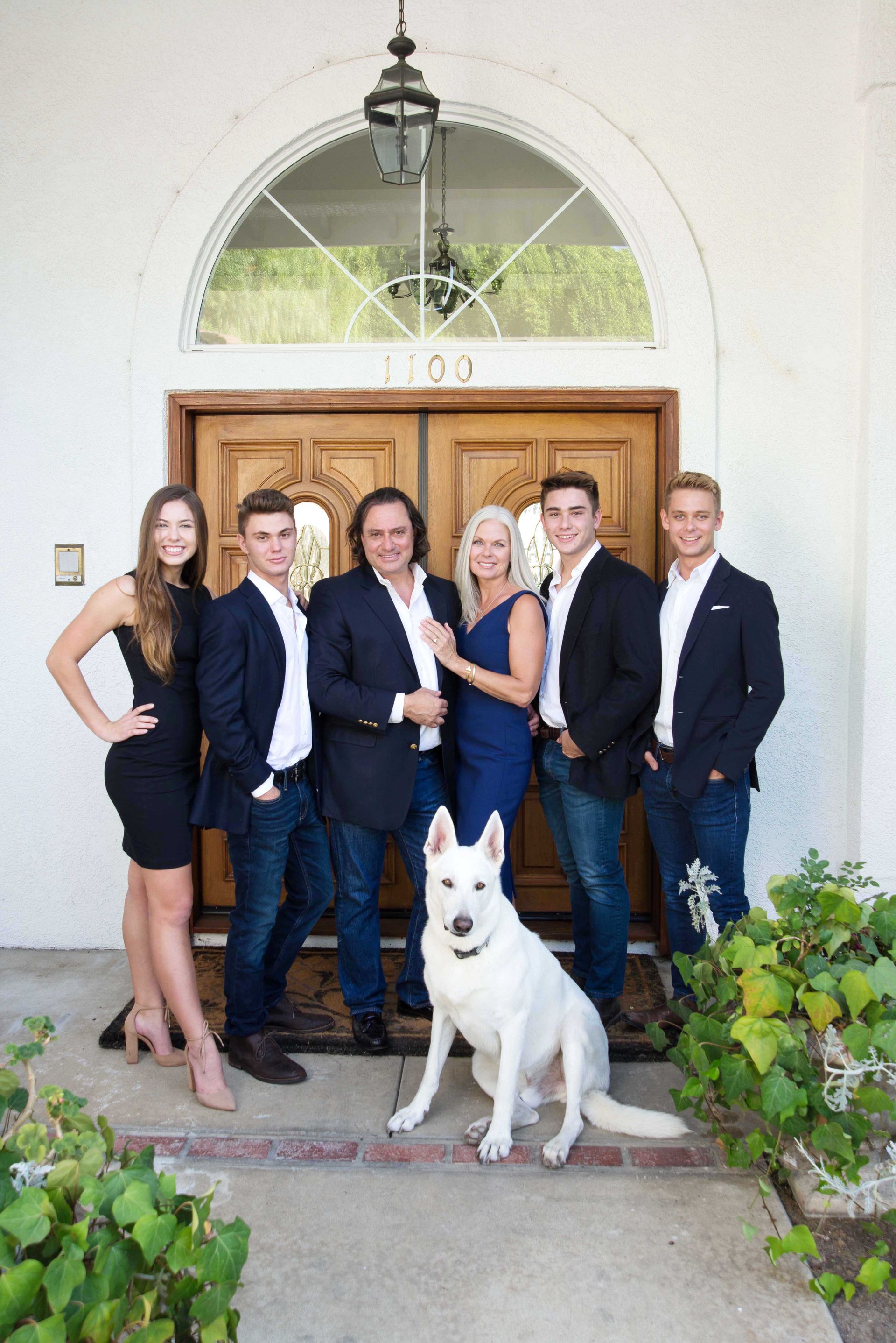Five people and a white dog posing in front of a wooden front door and arched window