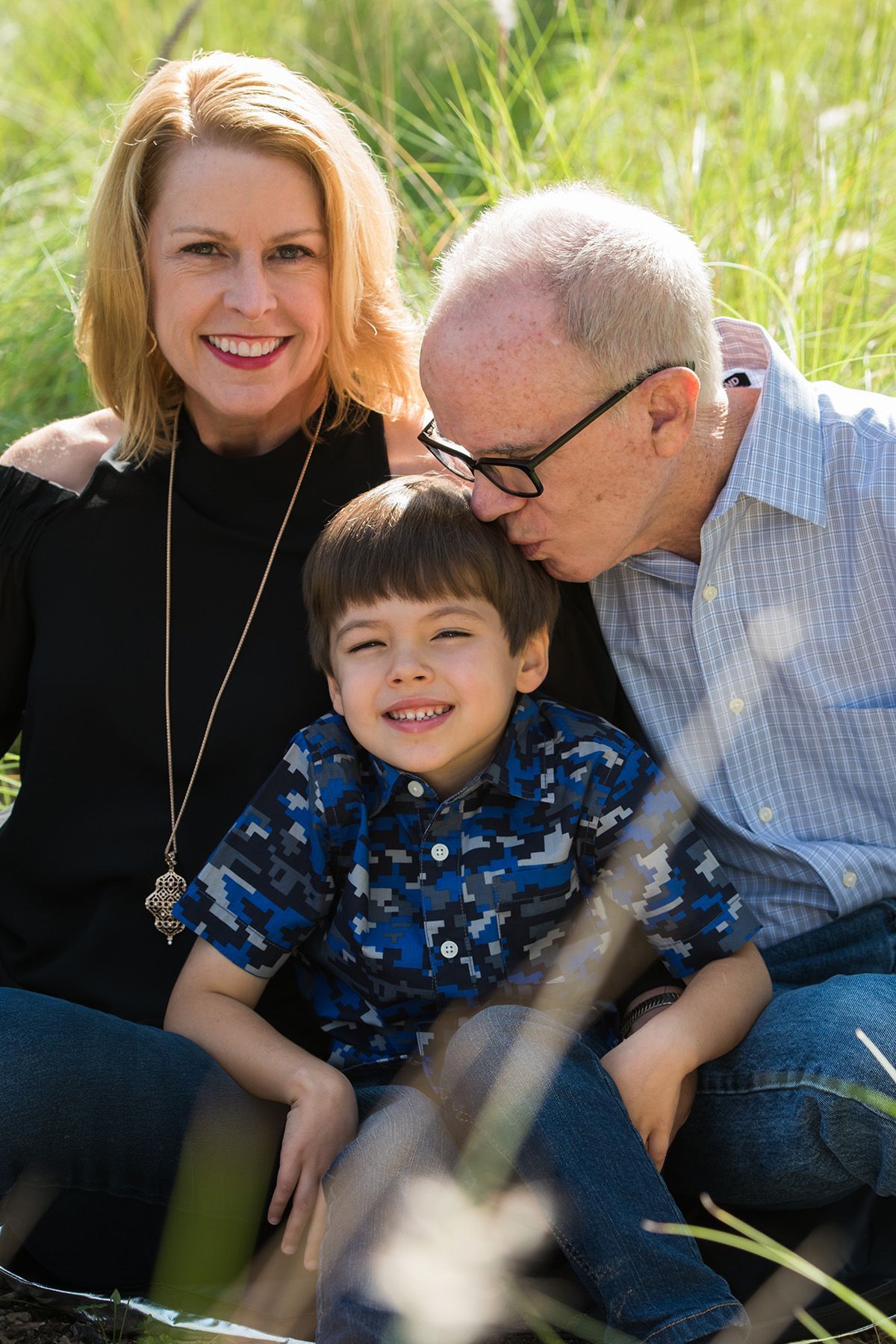 Family sitting together in tall grass, smiling at the camera.