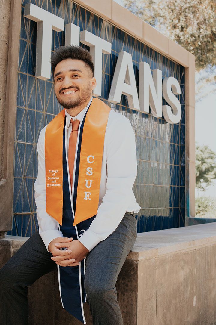 Man sitting in an orange stole in front of a TITANS sign, smiling outdoors