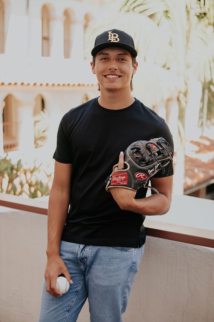Young man in a black T-shirt and cap holding a baseball glove and ball outdoors on a balcony