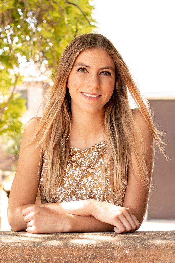Woman smiling with arms folded on a table in a bright outdoor setting