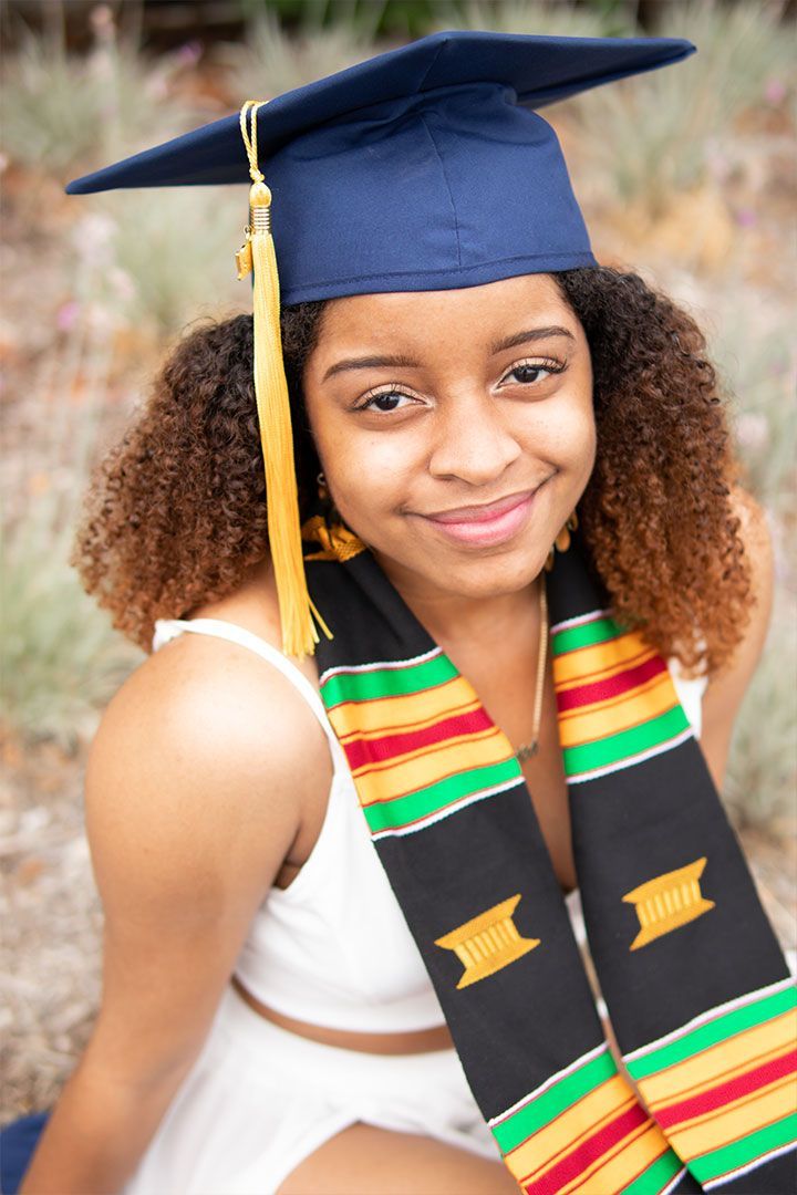 Graduate in blue cap and colorful stole smiling outdoors