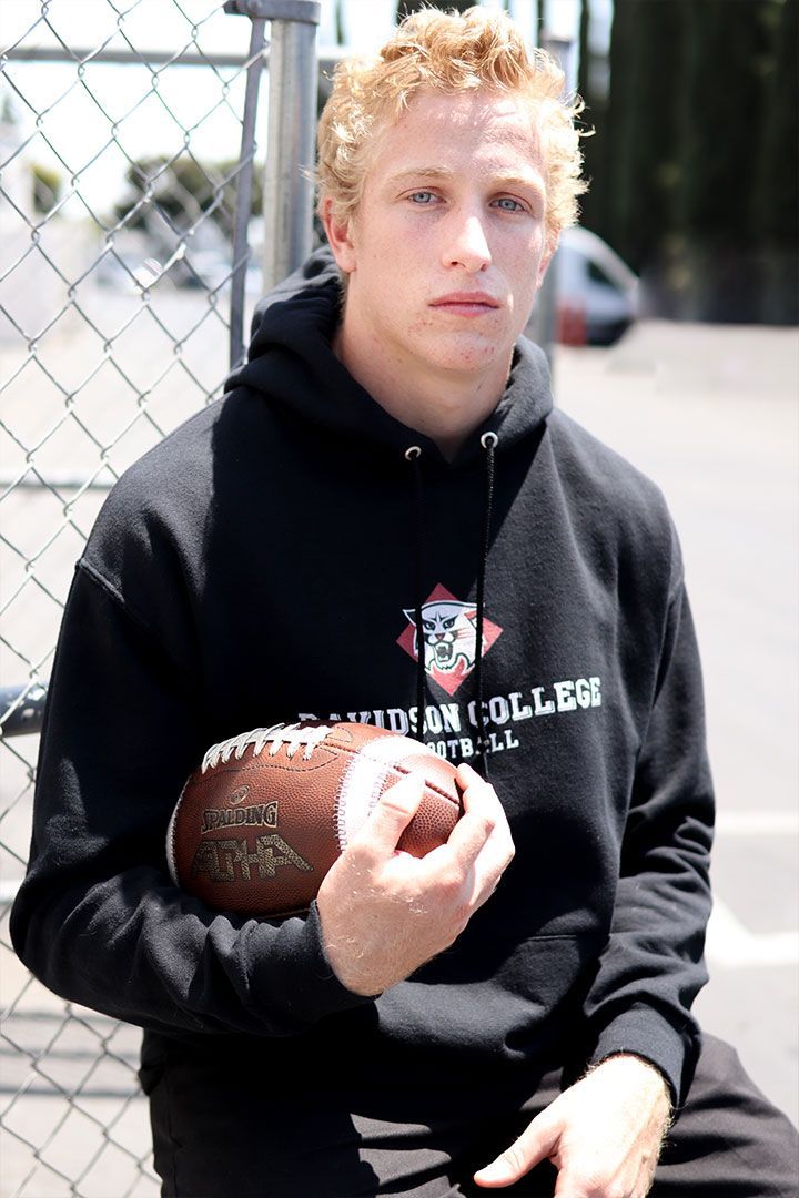Person in a black hoodie sitting outdoors, holding a football.