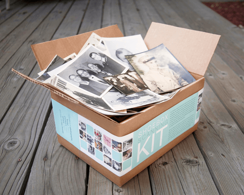 Cardboard box filled with printed photos and papers on a wooden deck