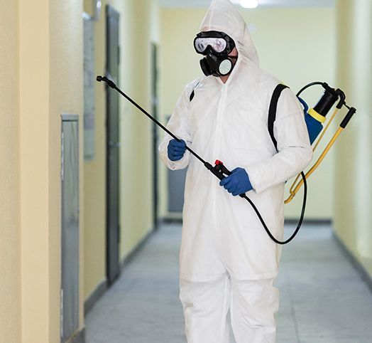 A man in a protective suit is spraying something in a hallway