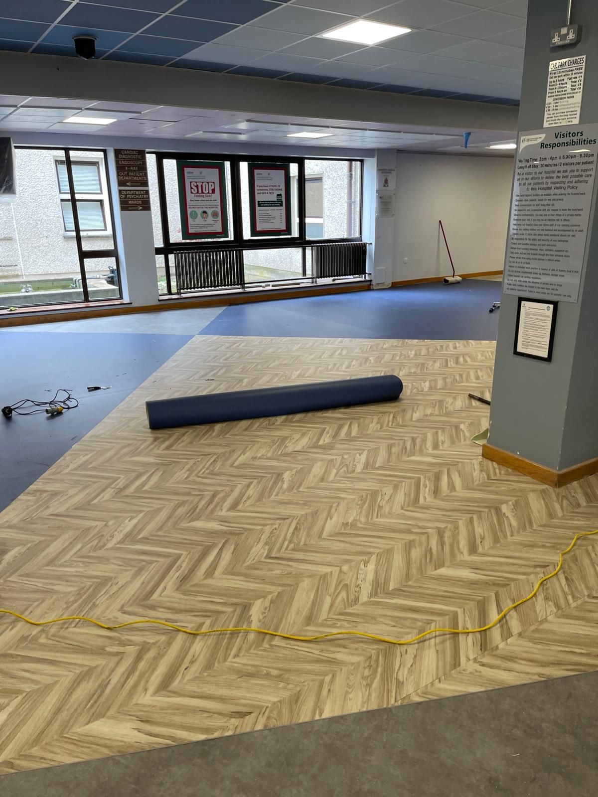 Room with wood-patterned flooring being installed; blue mat rolled out; yellow power cord runs across floor.