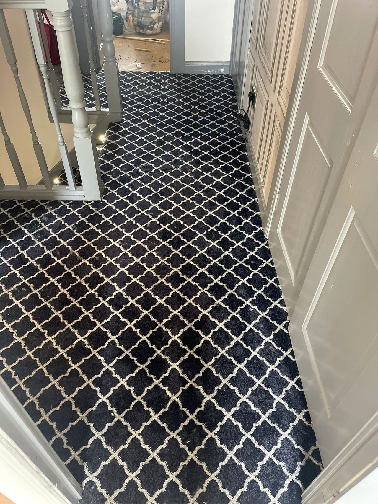 A hallway with a black and white carpet and stairs.