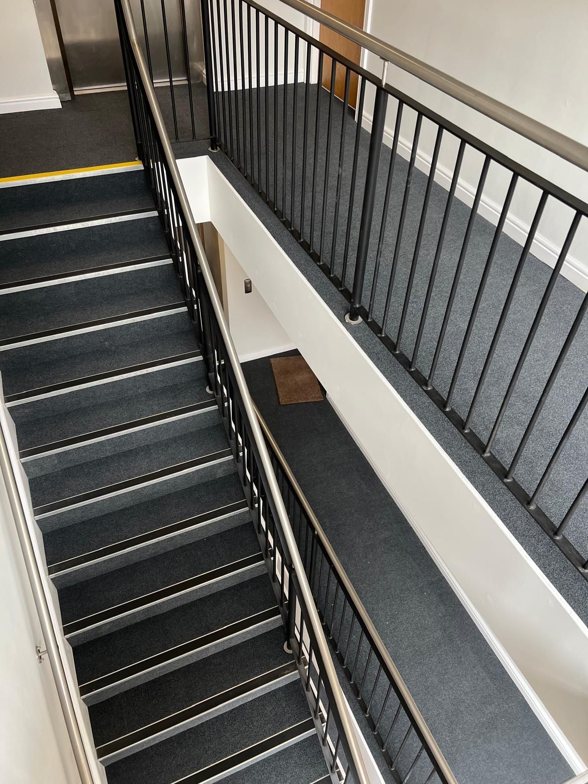 Staircase with black treads and gray carpeted runner, black metal railings, and white walls.
