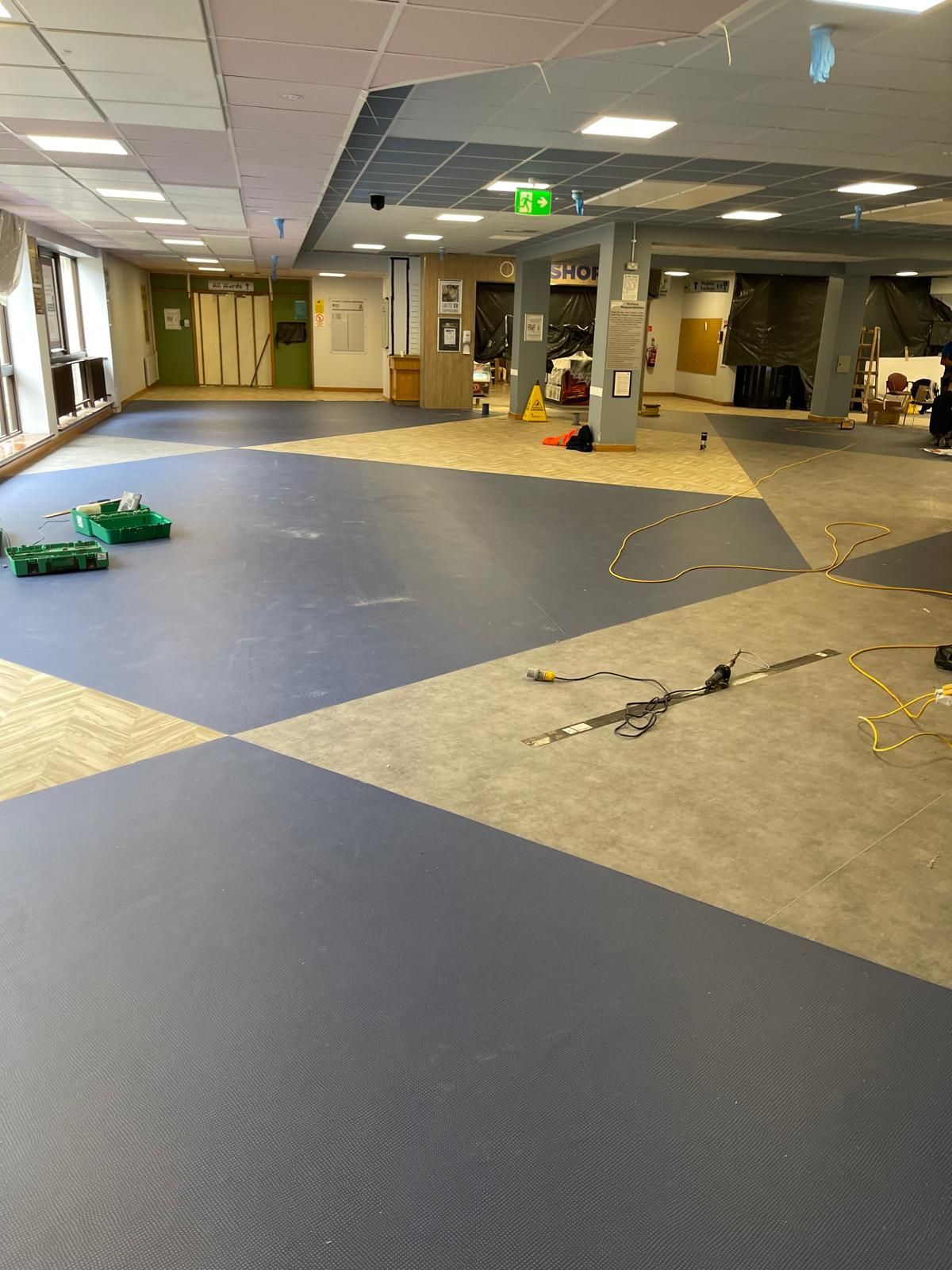 Indoor space with blue and beige floor tiles; robots and cables scattered around; doorways and lights visible.