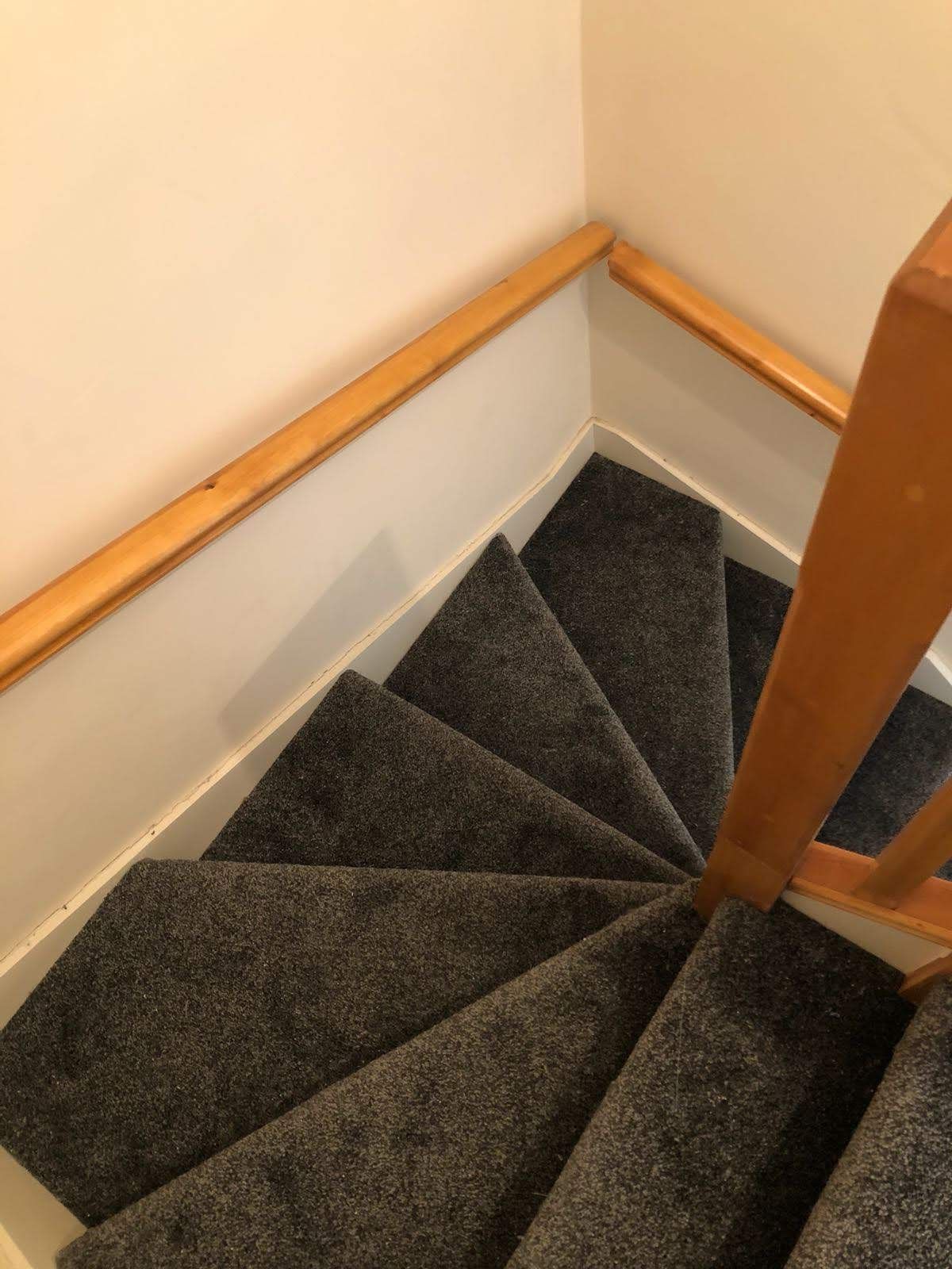 A spiral staircase with a wooden railing and a gray carpet.
