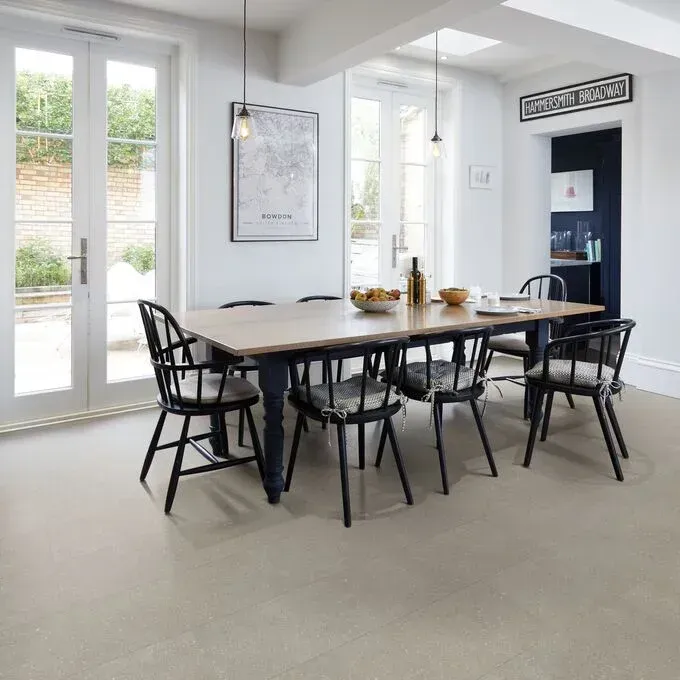 A light-filled dining room features a wooden table with six black spindle chairs, set against white walls and patio doors.