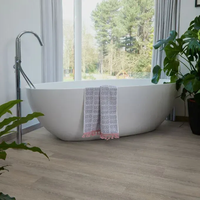 A bathtub in a bathroom next to a window and a plant.