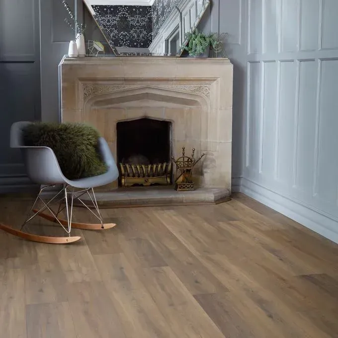A light grey room with a stone fireplace, a grey rocking chair with a dark green faux fur pillow, and light wood flooring.
